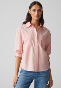 Helles rosa, knöpfbares Hemd mit Kragen, zwei Brusttaschen und umgeschlagenen 3/4-Ärmeln, aus einem weichen, strukturierten Stoff.
