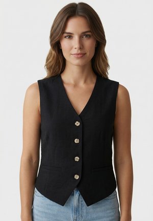Femme aux cheveux bruns ondulés portant un gilet noir sans manches boutonné et un jean bleu clair, face à un fond uni.