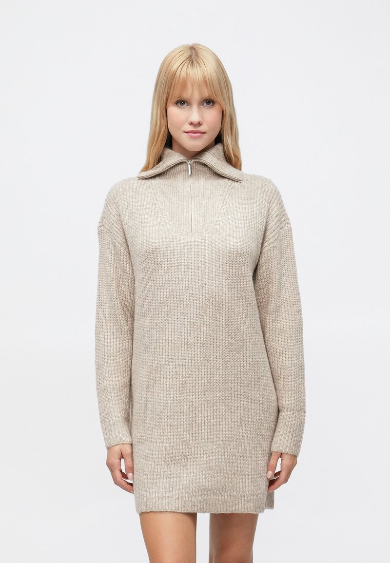 Rochie tricotată bej, cu guler înalt și fermoar până la piept, având mâneci lungi și croială lejeră. Material texturat cu modele ribbed.