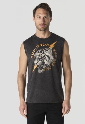 Hombre con camiseta sin mangas negra con gráfico de tigre rugiente y rayo, caracteres japoneses naranjas y texto "Salvaje y Libre".