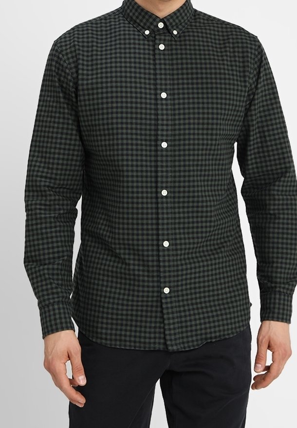 Muž oblečený v tmavě zelené a černé kostkované košili s dlouhým rukávem, s bílými knoflíky, v kombinaci s černými kalhotami.
