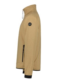 Chaqueta de cremallera color caqui con cuello alto, que presenta un parche de logo negro en el hombro y bolsillos laterales con cremallera, con acentos en negro en los puños.