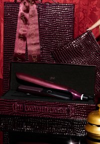 Paarse krokodillen-embosserde hoes met een bijpassende strik bevat een slanke, glanzende paarse haarstijltool met een donkere plaat, die subtiele branding toont.