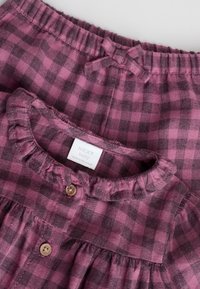 Robe à carreaux roses et noirs avec un col à volants, fermeture boutonnée et taille élastique. Étiquette visible : NEXT bébé.