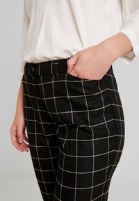Czarne spodnie w kratę z białym wzorem siatki, o eleganckim kroju, z bocznymi kieszeniami i płaskim paskiem w talii.