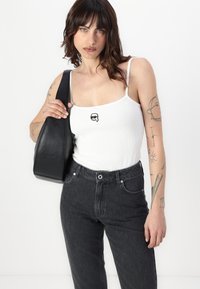 Melnas ādas pleca soma ar gludu tekstūru, valkāta ar baltu ribotu topu, kura priekšpusē ir neliels melns grafiskais attēls, un augstās vidukļa tumšām džinsu biksēm.