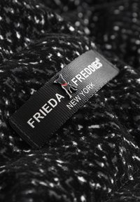 Czarny i biały teksturowany materiał z wyraźną etykietą z napisem "FRIEDA FREDDIES NEW YORK." Do etykiety przymocowane jest małe logo psa.