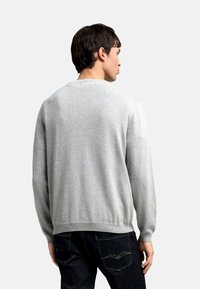 Suéter gris de manga larga y cuello redondo, con una textura suave. Combinado con unos vaqueros oscuros, mostrando un dobladillo acanalado en la parte inferior.