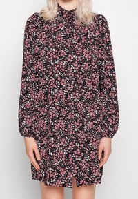 Schwarzes Blumenkleid mit langen Ärmeln, das mit rosa und weißen Blumen verziert ist, einem plissierten Design und einer Knopfleiste an der Vorderseite sowie einem Schlitz am Saum.