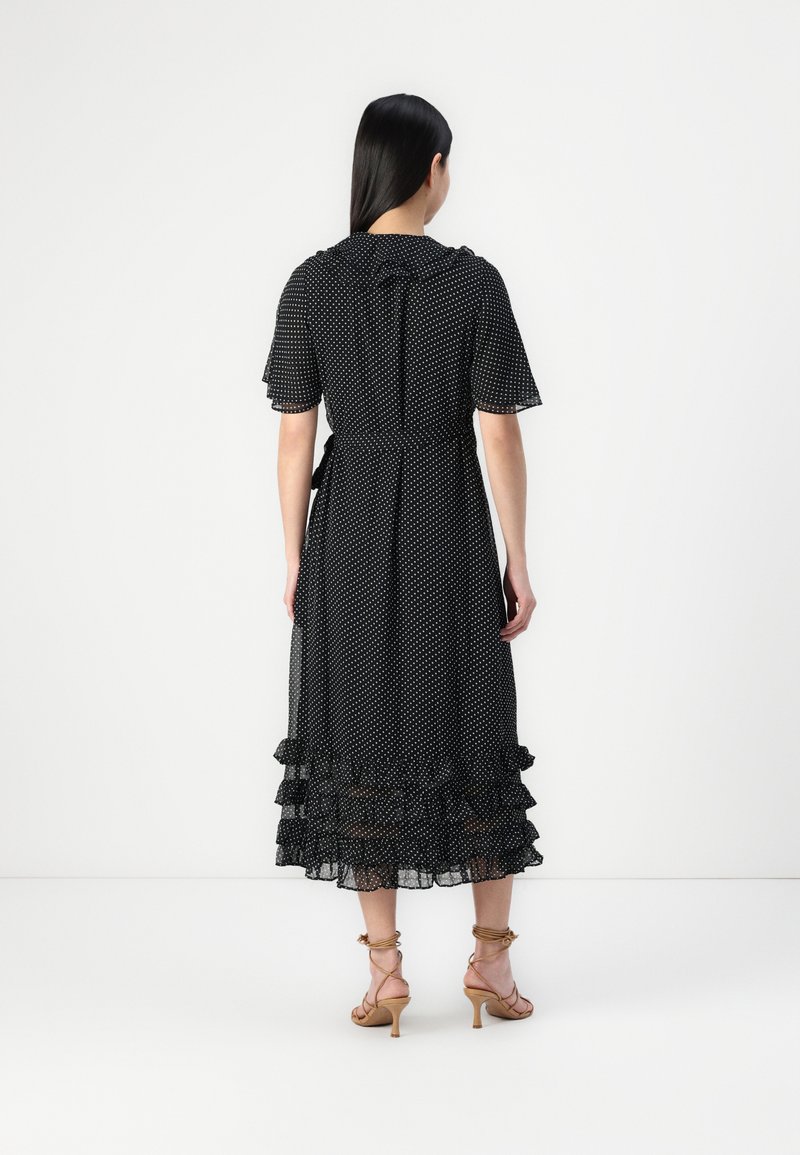 Robe noire à pois en tissu transparent, dotée de manches courtes évasées, d'une taille ceinturée et d'un ourlet à volants en étages.