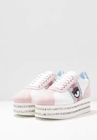 Plattform sneakers med ovandel i vitt läder, rosa mockadetaljer och en glittrig silverfärgad mellansula. Har ett dekorativt ögonmotiv på sidan.