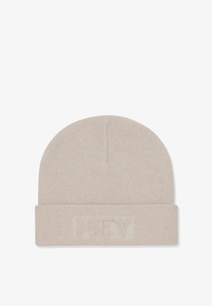 Bonnet en tricot crème avec un revers replié, présentant un tissu texturé et un logo brodé subtil sur le devant. Design doux et ajusté.