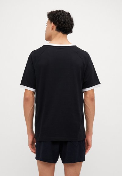 T-shirt preto de manga curta com colarinho e punhos brancos em contraste, apresentando um corte descontraído e textura suave. Vista traseira mostrando mangas raglan.