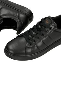 Černé kožené nízké tenisky s kulatou špičkou, texturovaným povrchem, černými tkaničkami a značkovým akcentem po straně. Gumová podrážka s protiskluzovou úpravou.