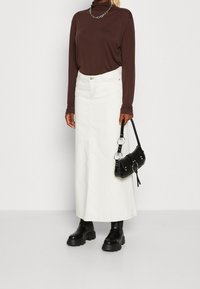 Vit denim maxikjol, lång brun långärmad topp, svarta kängor med tjock sula och en svart handväska med cirkulära metallaccenter.