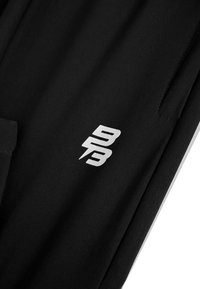 Zwarte sportkleding met een gladde textuur en een opvallend wit logo aan de zijkant. Het ontwerp heeft een minimalistische stijl en geen patronen.