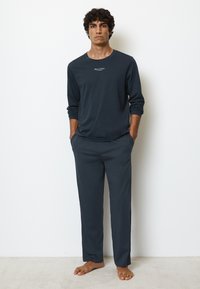 Set di abbigliamento da casa blu scuro composto da una maglia a maniche lunghe e pantaloni larghi. Tessuto morbido, design minimal e tasche laterali sui pantaloni.