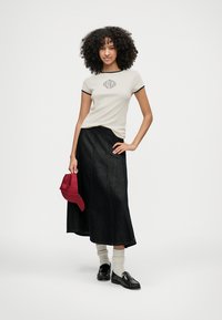 Tricou bej deschis cu tiv și logo bleumarin, asortat cu o fustă din denim negru. Pantofi loafer negri și șapcă roșie completează ținuta, cu șosete albe.