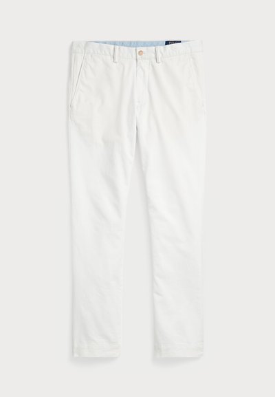 Baltās kokvilnas chinos bikses ar gludu priekšu, jostu cilpām, divām sānu kabatām un vienu aizmugures kabatu. Gluda tekstūra ar taisnu kāju.