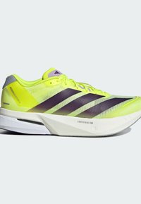 Scarpe da corsa gialle vivaci con accenti viola, parte superiore in rete leggera, design elegante e un'intersuola in schiuma bianca etichettata 'LIGHTSTRIKE PRO'.