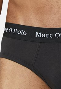 Schwarze Baumwollunterhose mit einem weichen elastischen Bund, der das Logo "Marc O'Polo" in kontrastierendem weißen Text trägt. Glatte Textur, enganliegendes Design.