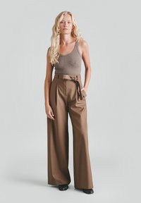 Brązowe spodnie o szerokich nogawkach z wysokim stanem i paskiem do wiązania, zestawione z dopasowanym brązowym topem na ramiączkach. Gładka faktura, minimalne zdobienia.