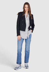 Cropped navy double-breasted jacket over a white and black striped shirt, light blue jeans, and gray athletic shoes.