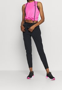 Fuchsia ärmlös crop top, svarta tapered joggers med elastiska muddar och svarta sneakers med rosa accenter, med en minimalistisk design.