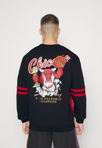 Sweatshirt noir avec un graphisme vif d'un taureau tenant un trophée et un ballon de basket, avec des rayures rouges sur les manches et un texte en gras.