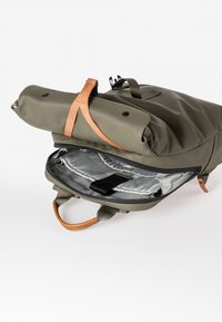 Zaino verde oliva con dettagli in pelle. Presenta una chiusura a roll-top, un interno foderato grigio e una cinghia per fissare il contenuto.