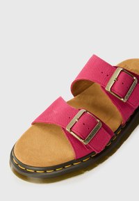 Sandal roz din piele cu două curele reglabile, catarame din metal și o talpă interioară căptușită bej. Tălpica din cauciuc are cusături galbene.