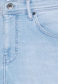 Los jeans de denim azul claro presentan un diseño clásico de cinco bolsillos, con un botón plateado y sutiles detalles de costura. Tejido suave y ligeramente texturizado.