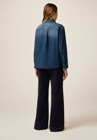 Blue denim jacket with a back pleat, buttoned cuffs, and classic collar, paired with navy wide-leg trousers. Smooth texture and casual design.