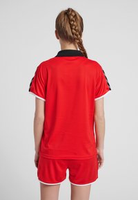 Red sports jersey and matching shorts with black collar and accents. Made of breathable fabric, featuring short sleeves and a relaxed fit.