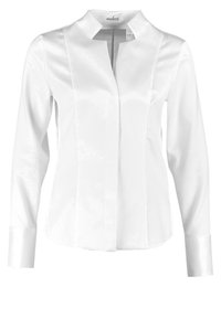 Vit långärmad blus med mandarinkrage. Tillverkad av glänsande tyg, med vertikala sömmar och en enkel design. Manschetterna är noggrant sydda.