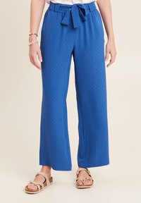 Pantaloni larghi blu con un motivo testurizzato, caratterizzati da una vita legata e una vestibilità morbida. Abbinati a sandali marroni.