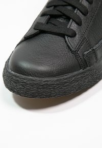 Schwarze Ledersneaker mit abgerundetem Zehenbereich, strukturiertem Gummisohle und flachen Schnürsenkeln. Das Material wirkt glatt mit dezenten Nähdetails.