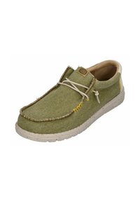 Scarpa in tessuto verde con superficie a struttura, bordi cuciti e suola in gomma beige. Presenta un sistema di allacciatura semplice e una patch con logo sulla parte superiore.