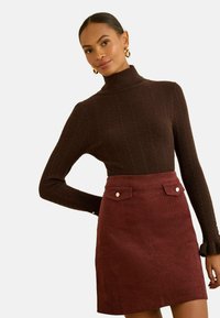 Pulover turtleneck ribbed maro, cu un design ajustat, asortat cu o fustă mini din catifea bordeaux cu buzunare frontale și accentuări cu nasturi.