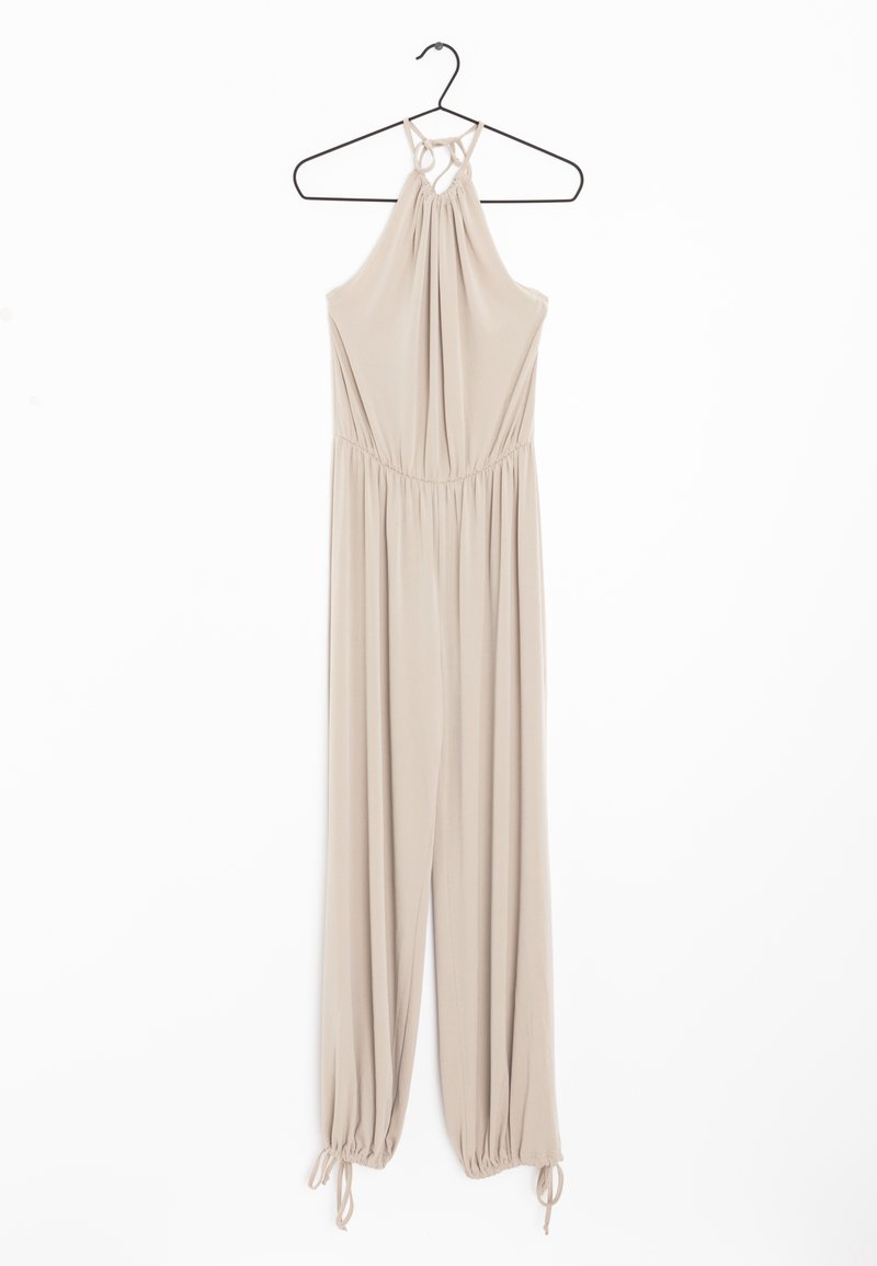 Combinaison beige sans manches avec col licou et bas des jambes froncés, suspendue à un cintre noir sur un fond blanc.