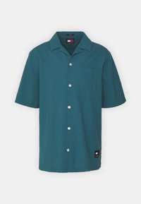 Kortermet skjorte med knapper i teksturert teal-stoff, med en enkelt brystlomme og hvite knapper; merkeetikett på kanten.