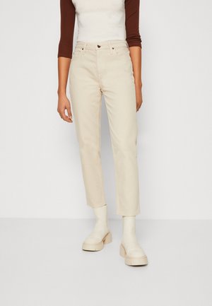 Jeans de algodón beige con corte recto, cintura de media altura y cierre de botón. Combinados con botines crema.