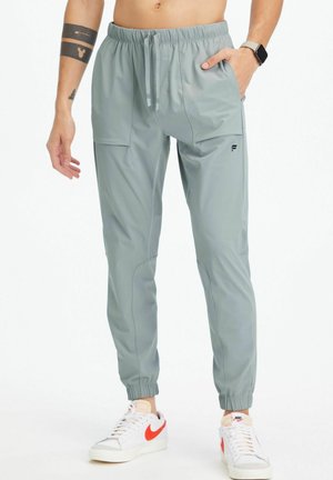 Lichtgrijze sportieve joggers met een elastische tailleband, zijzakken en een aangesloten enkels, gemaakt van een gladde, lichte stof.