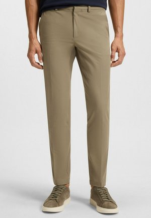 Beige Slim-Fit-Hosen aus einem glatten Stoff, ausgestattet mit Seitentaschen, Gürtelschlaufen und einem schlanken Design, kombiniert mit grauen Sneakers.