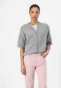 Cardigan grigio a maniche corte con collo rotondo, chiusura a bottoni e texture morbida, abbinato a jeans rosa chiaro. Design semplice, colore neutro.