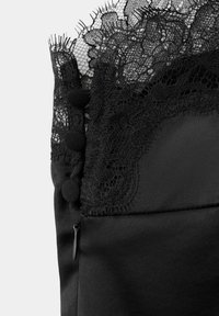 Tissu noir avec un galon en dentelle complexe, des boutons recouverts de tissu et une petite fermeture éclair sur le côté d’un vêtement.