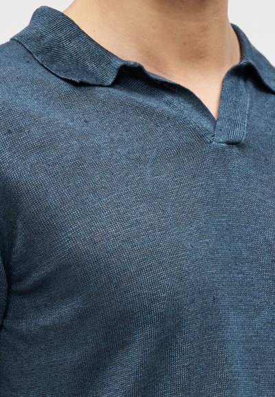 Polo-skjorte i mørk teal, teksturert stoff, kort krage og v-utringning. Har et subtilt strikkemønster over hele.