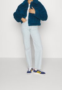 Fuzzy teal jacka med krage och två bröstfickor, tillsammans med ljusblå raka jeans och marinblå sneakers med gula ränder.