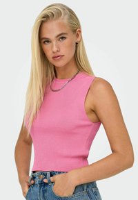 Canotta aderente a coste di un brillante color rosa con scollatura alta e senza maniche, abbinata a pantaloni corti di jeans a vita alta.