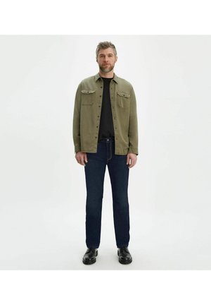 Olivgrön skjorta med knappar och två bröstfickor, svart t-shirt med rund hals under, mörkblå jeans och svarta skor. Enkel design med klassisk passform.